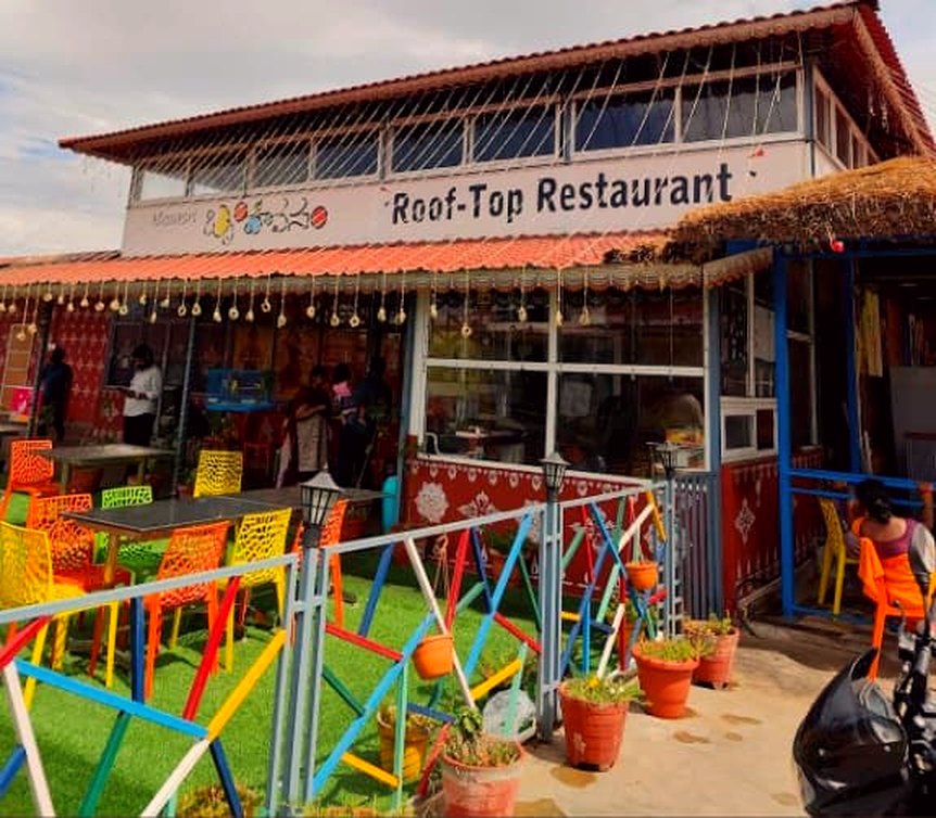 The terrace of Brindavanam seen from the walkway, with the terracotta tiled roof, the hand-painted Roof-Top Restaurant sign, the multicoloured steel railing and rows of plastic chairs on artificial grass.